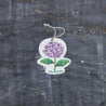 Top view of an eco-friendly cellulose pop-up kitchen sponge with hanging cord, featuring a lovely purple hydrangea design. This sustainable cleaning tool lies completely flat when dry for compact storage, then expands significantly when wet for optimal absorbency. Crafted from biodegradable plant-based cellulose, the sponge showcases a beautiful floral pattern that adds elegance to your kitchen while being gentle on the environment. 