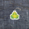 An eco-friendly cellulose pop-up kitchen sponge shown in top view, featuring a charming Frog Prince design. With an attached hanging cord for convenience, this biodegradable cleaner lies flat when dry and expands significantly when wet, combining playful aesthetics with practical cleaning performance.