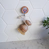 The wooden dish brush hangs on white tile walls.