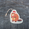 Top view of an eco-friendly cellulose pop-up kitchen sponge with hanging cord, featuring an adorable holiday beaver design wearing a red Santa hat and holding a red gift. This sustainable cleaning tool transforms from completely flat when dry to fully expanded when wet, combining festive cheer with practical functionality. Made from biodegradable plant-based cellulose, the seasonal sponge adds holiday spirit to your kitchen routine while being environmentally responsible.