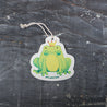 An eco-friendly cellulose pop-up kitchen sponge shown in top view, featuring a charming Frog Prince design. With an attached hanging cord for convenience, this biodegradable cleaner lies flat when dry and expands significantly when wet, combining playful aesthetics with practical cleaning performance.