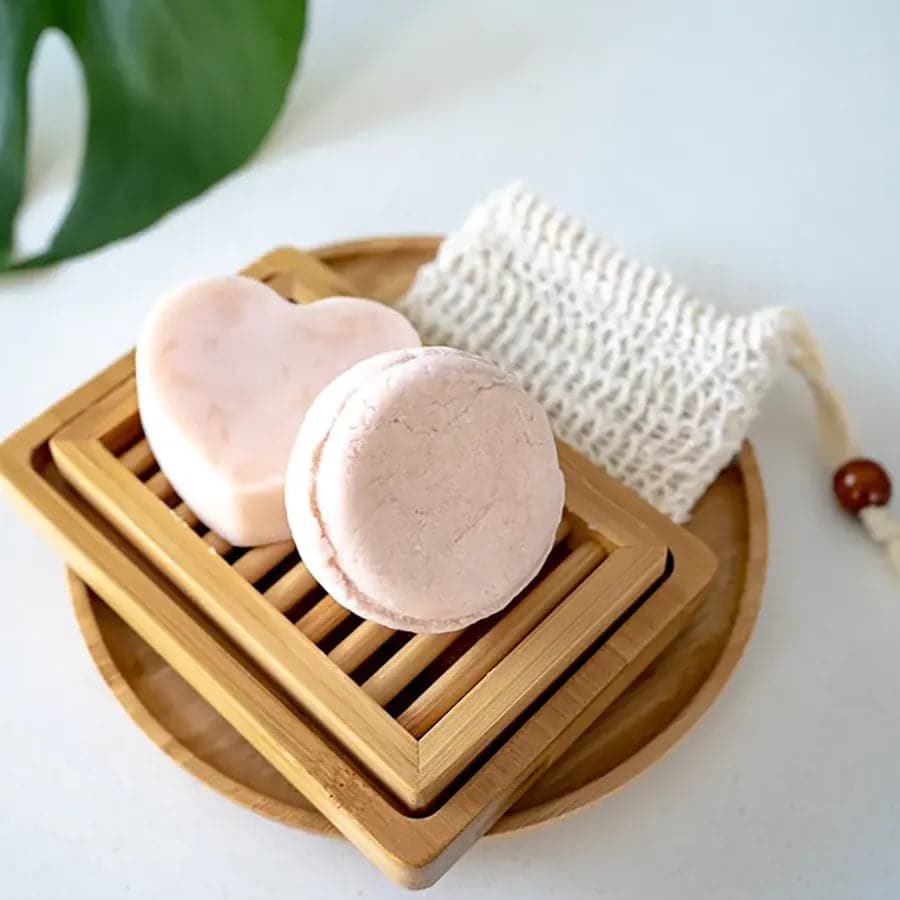 Nourishing shampoo and conditioner bar on top of bamboo self draining soap dish and loofah soap bag.