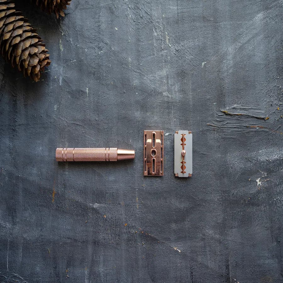 Disassembled plastic free rose gold safety razor with single blade.
