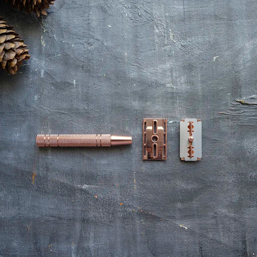 Disassembled plastic free safety razor with single blade in rose gold.
