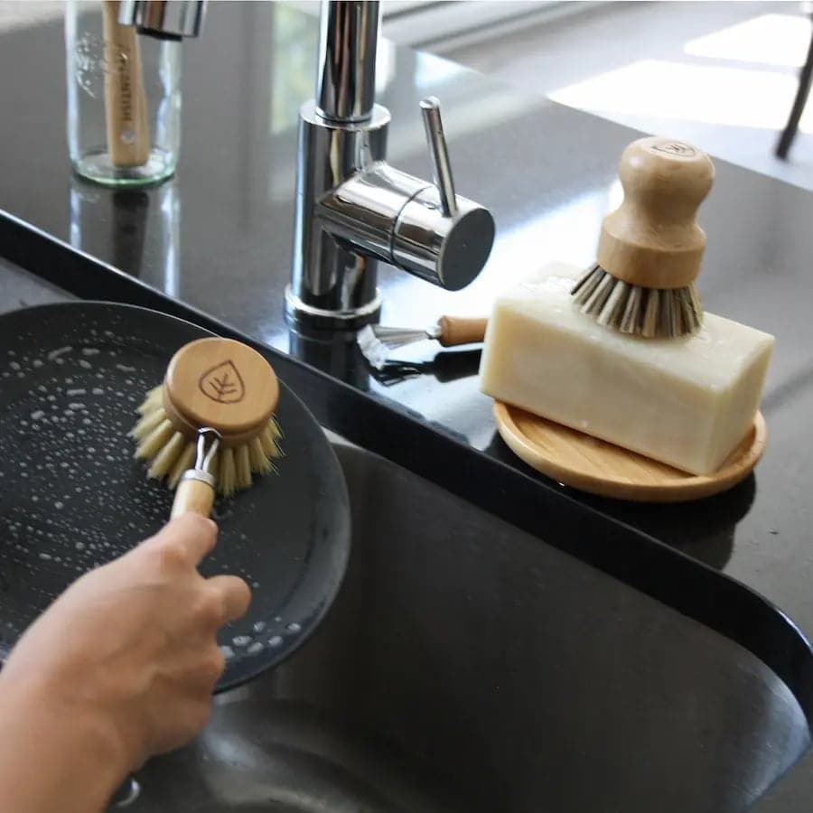 Using sisal dish brush on plate. Pot scrubber and solid dish soap brick on ledge of the sink.