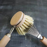 Brush cleaner brushing through sisal bristles of kitchen dish brush.