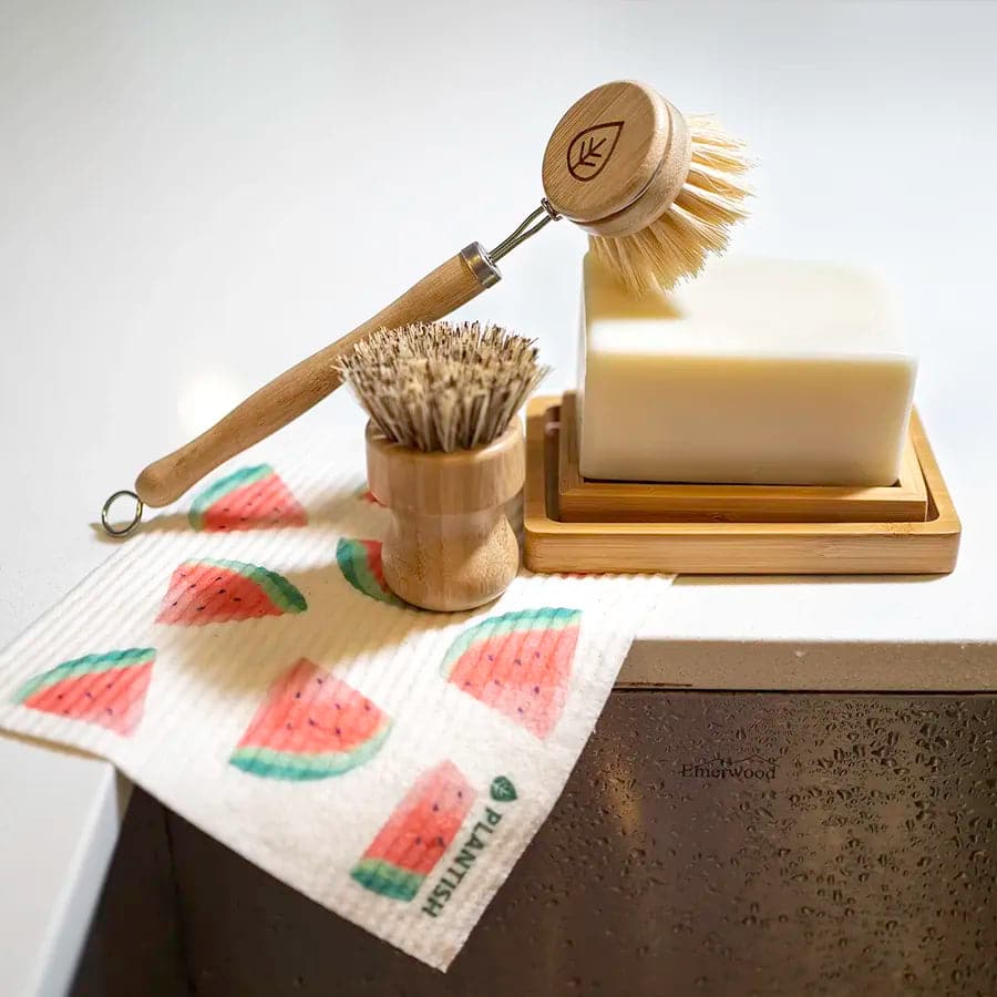 Sisal dish brush, sisal and palm pot scrubber and solid dish soap brick on top of watermelon reusable dishcloth.
