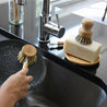 Using sisal dish brush to clean plate. Sisal and palm pot scrubber on top of solid dish soap bar.