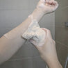 Using loofah soap bag with soap bar inside to lather soap onto skin.